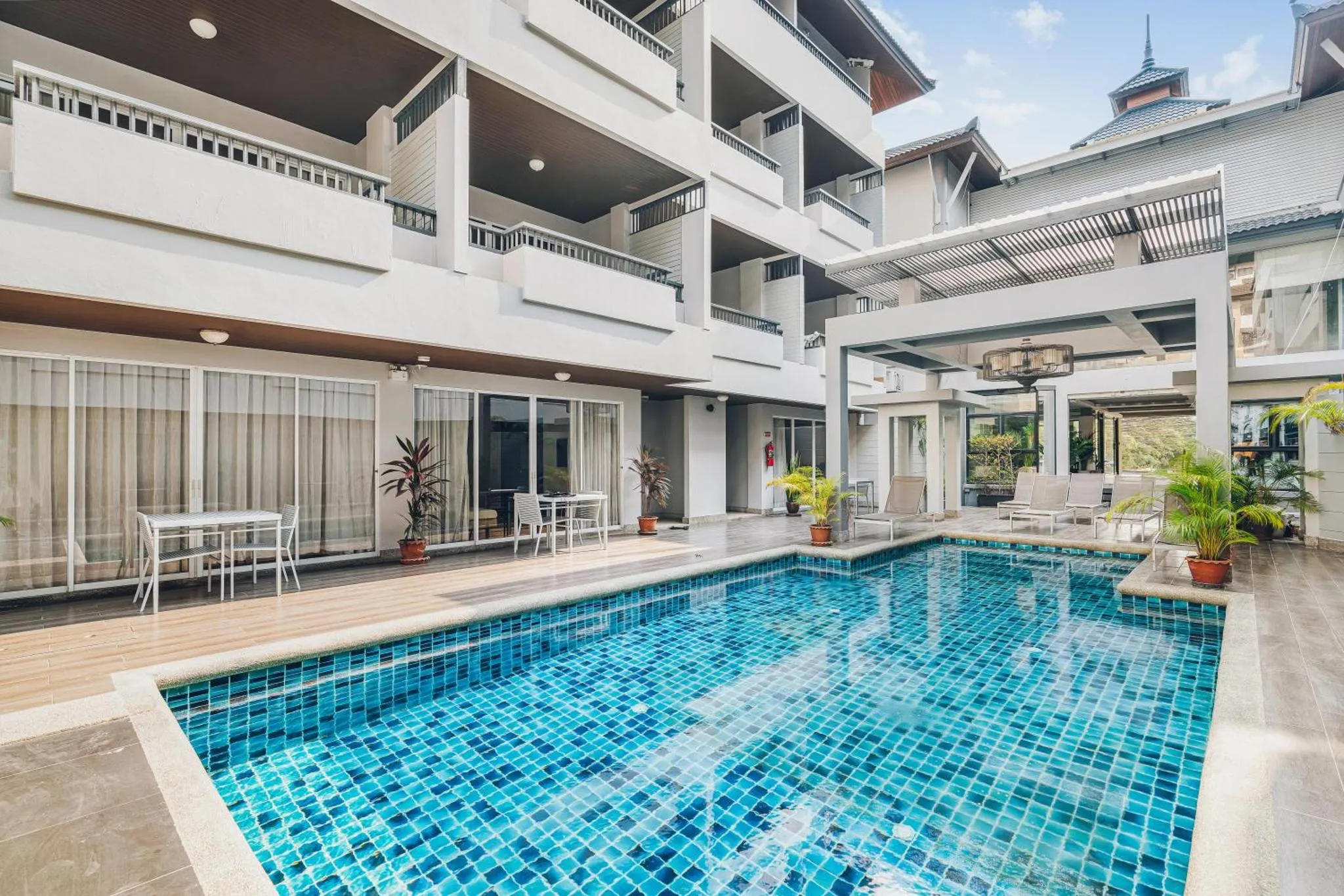 Une piscine rectangulaire est entourée d'une terrasse avec des transats et des tables.