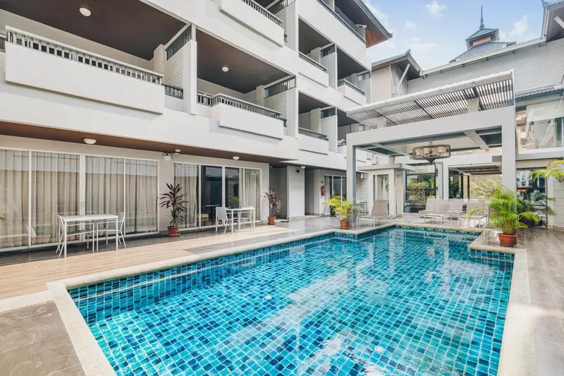 Une piscine rectangulaire est entourée d'une terrasse avec des transats et des tables.