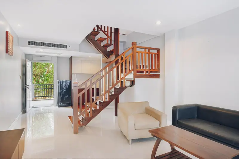 Un salon clair avec un canapé et un fauteuil face à un escalier en bois.