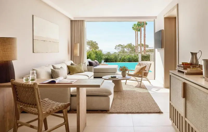 Espace de vie lumineux avec canapé, table basse et vue sur une piscine.