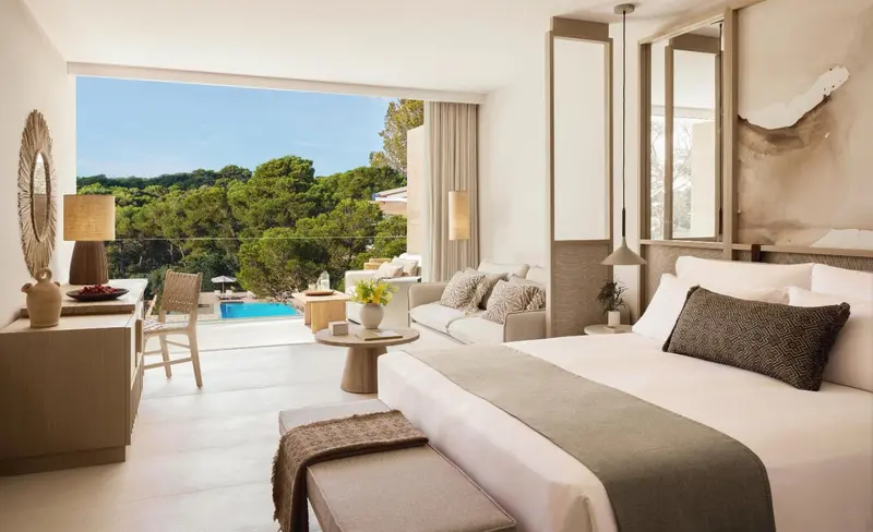 Une chambre lumineuse avec un grand lit et un coin salon donnant sur une vue verdoyante.