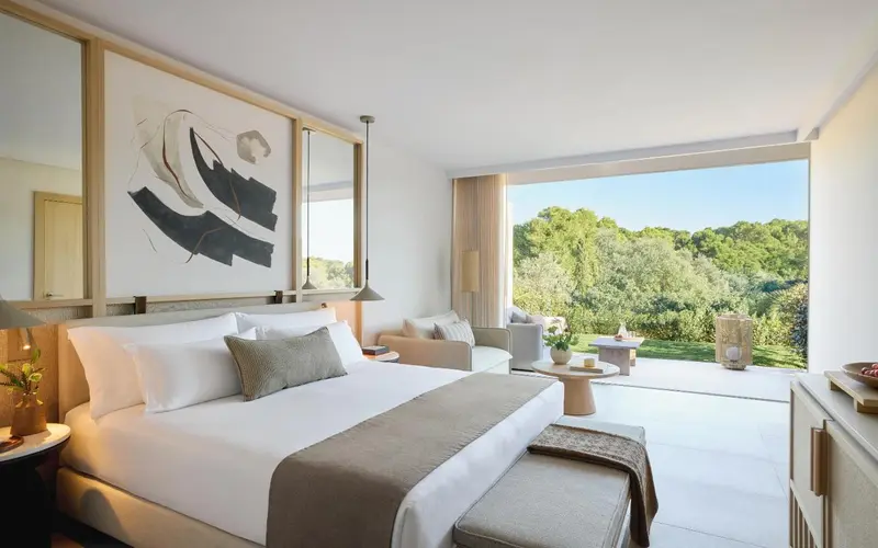 Une chambre lumineuse avec un grand lit et un espace salon donnant sur une vue verdoyante.