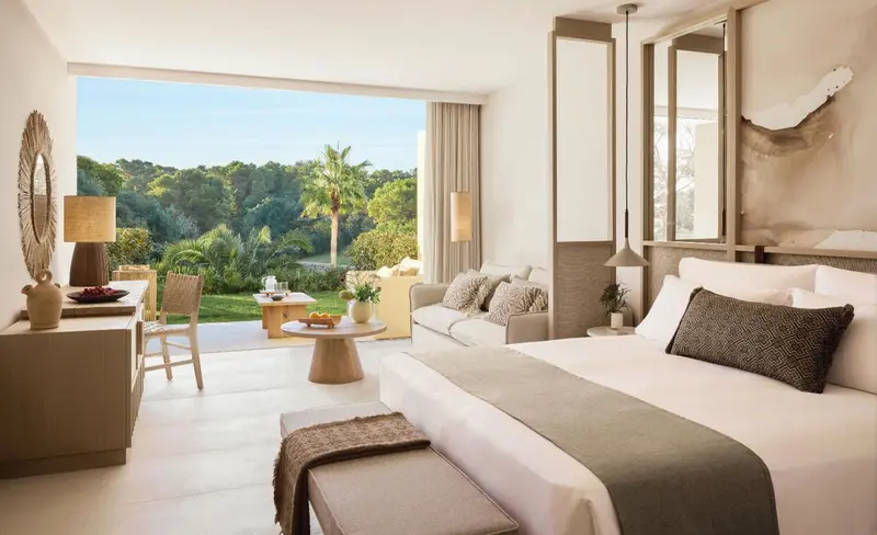 Une chambre lumineuse avec un grand lit et un canapé donnant sur une terrasse et une végétation luxuriante.