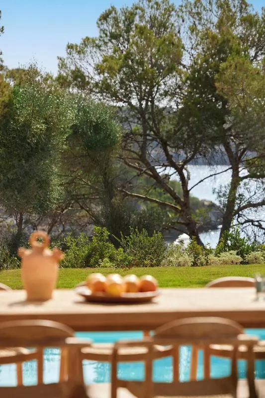 Une table en bois avec des fruits est mise en scène devant une piscine et une vue sur la mer.