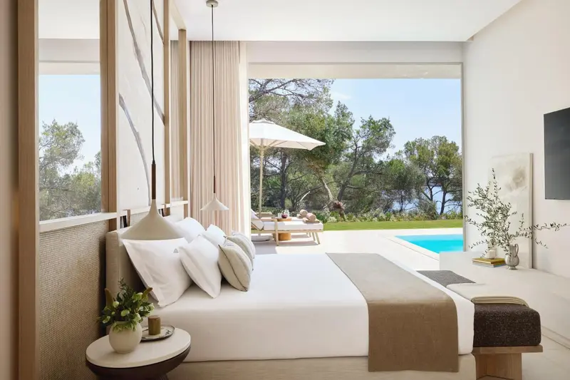 Une chambre lumineuse avec un grand lit donnant sur une piscine et une végétation luxuriante.