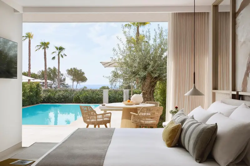 Une chambre lumineuse s'ouvre sur une terrasse avec vue sur une piscine et la mer.
