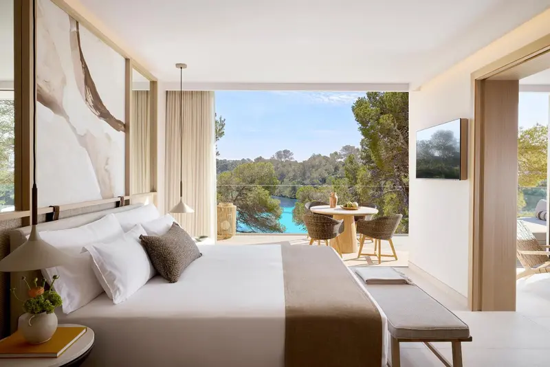 Une chambre lumineuse avec un grand lit et un coin repas donnant sur une vue verdoyante.