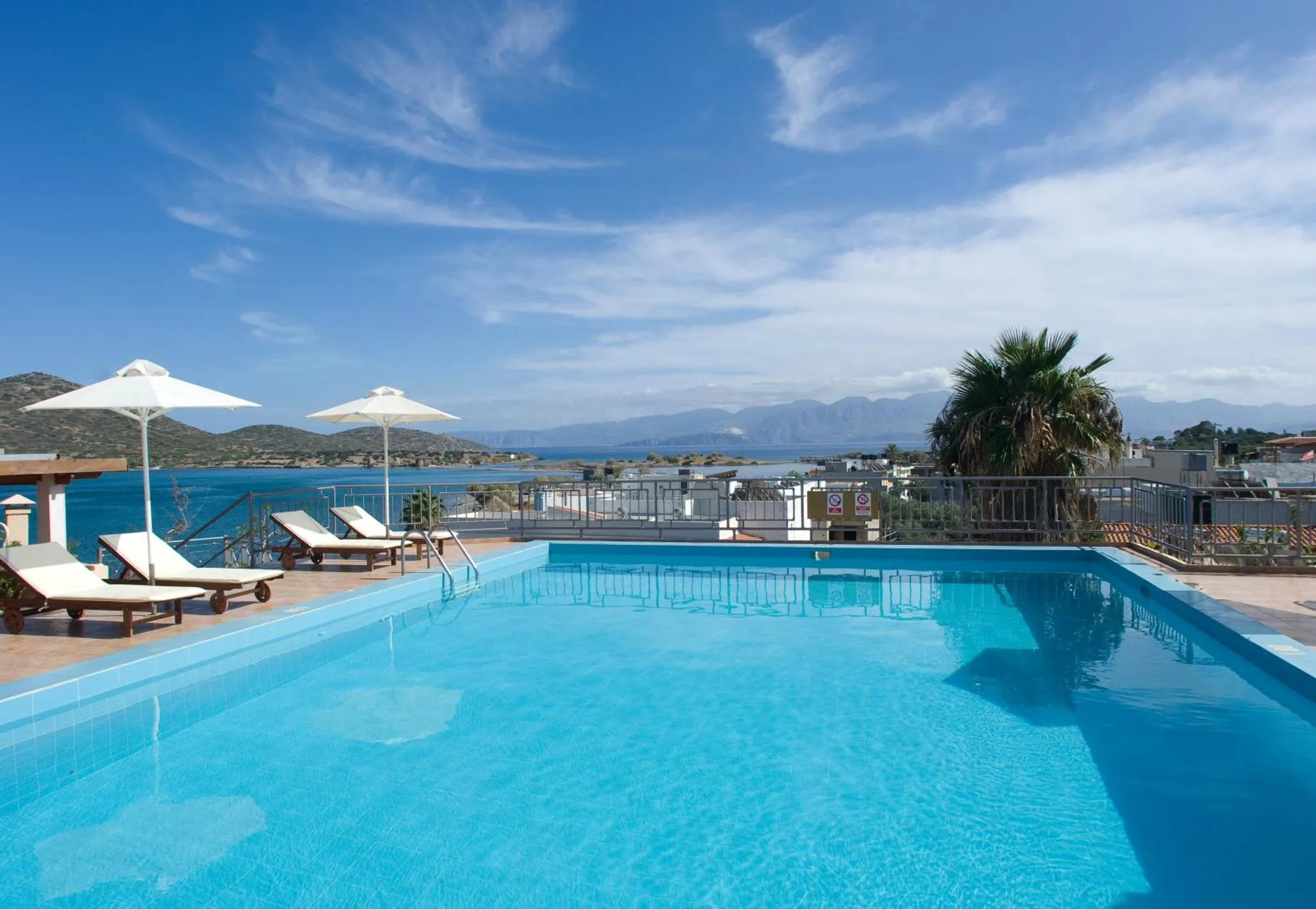 Transats blancs disposés au bord d'une piscine bleue avec vue sur la mer.