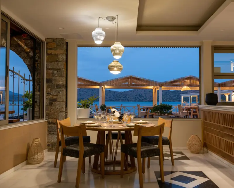 Une table ronde est mise pour un repas dans une salle lumineuse avec vue sur la mer.