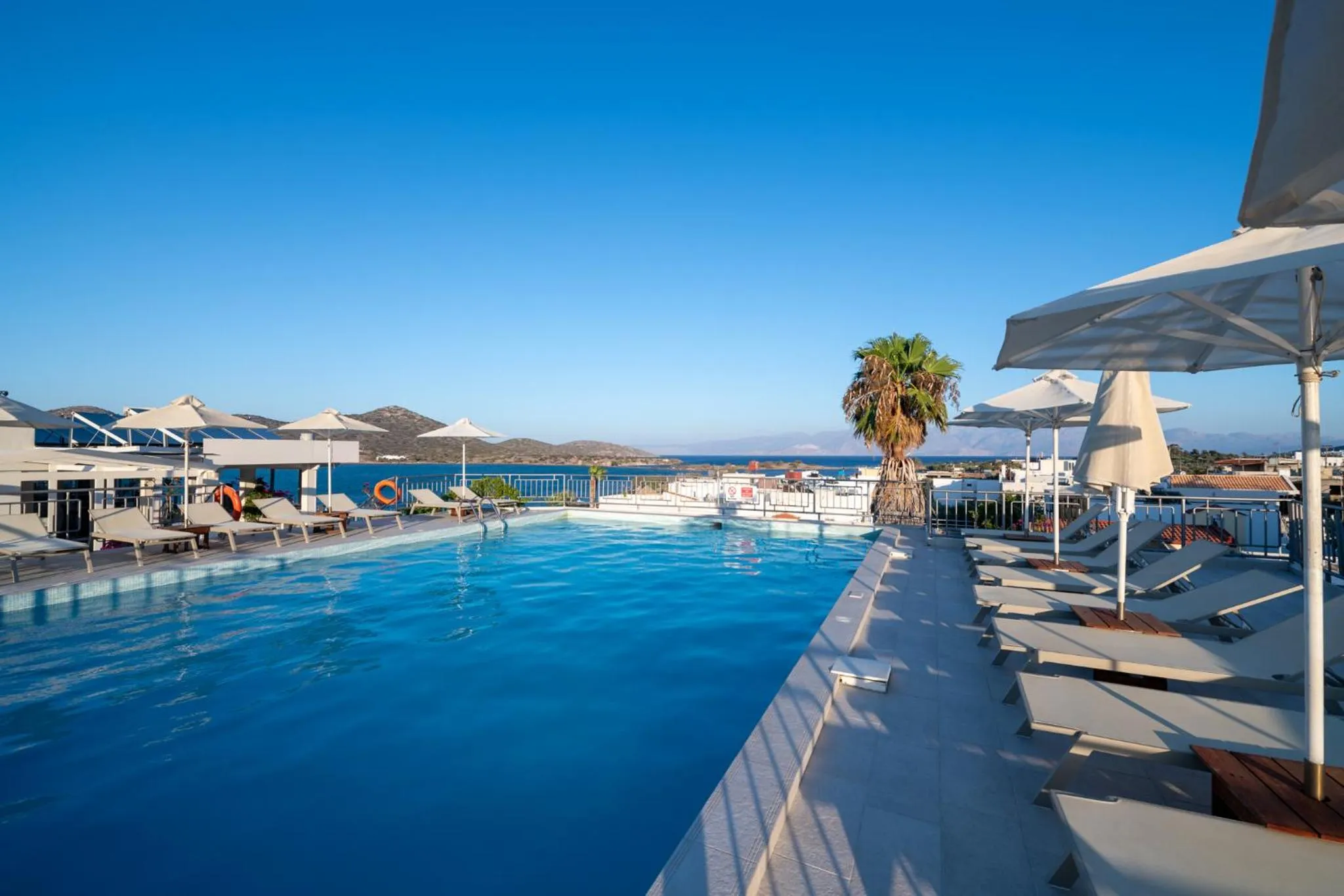 Transats blancs disposés autour d'une piscine à débordement avec vue sur la mer.