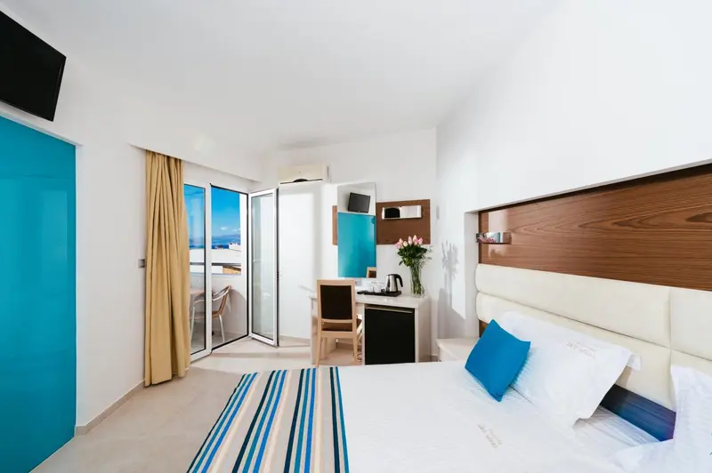 Chambre lumineuse avec un lit double et un balcon offrant une vue sur la mer.