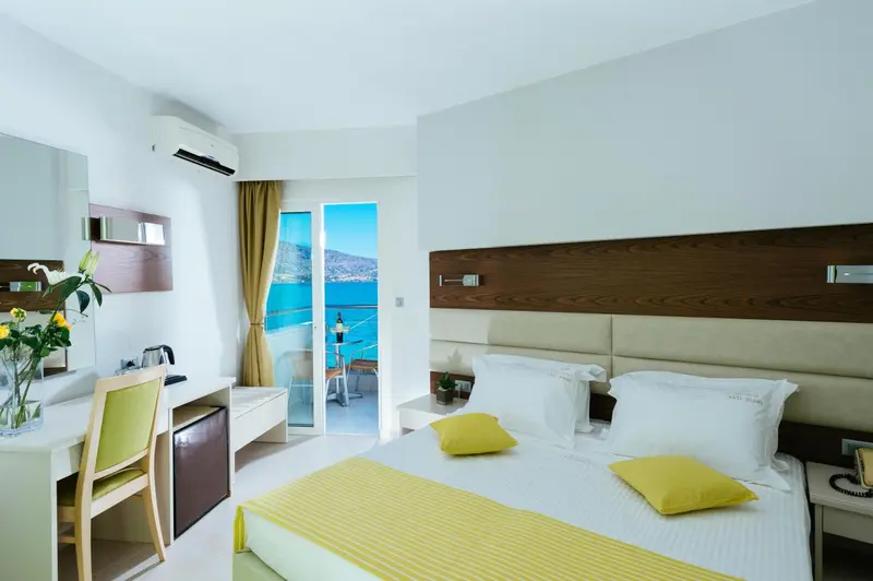 Chambre lumineuse avec un lit double et une vue sur la mer depuis un balcon.