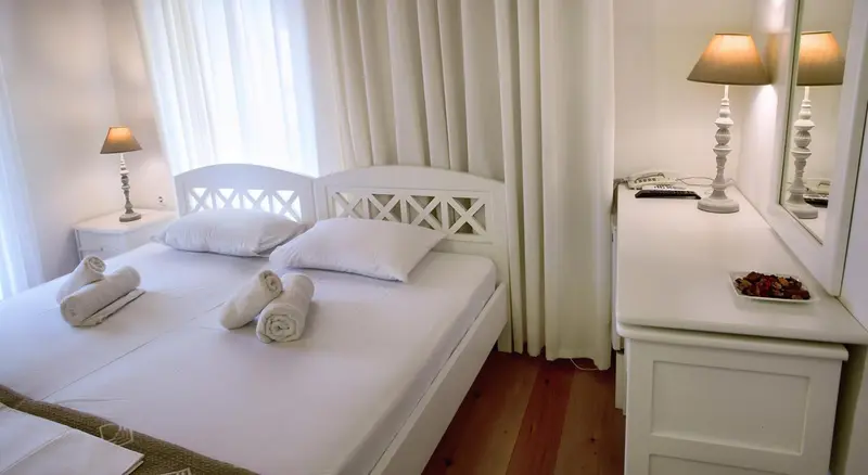 Une chambre lumineuse avec un lit blanc et des meubles clairs.