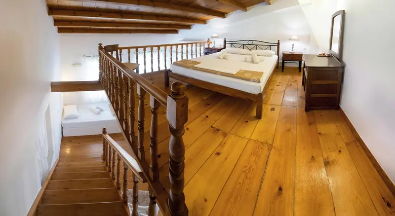 Une chambre mansardée lumineuse avec un lit double et un escalier en bois.