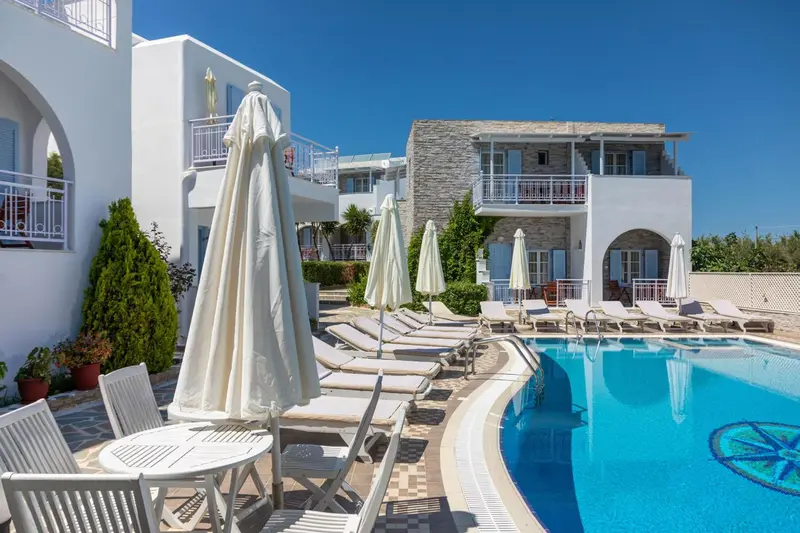 Transats et parasols bordent une piscine devant un bâtiment blanc.