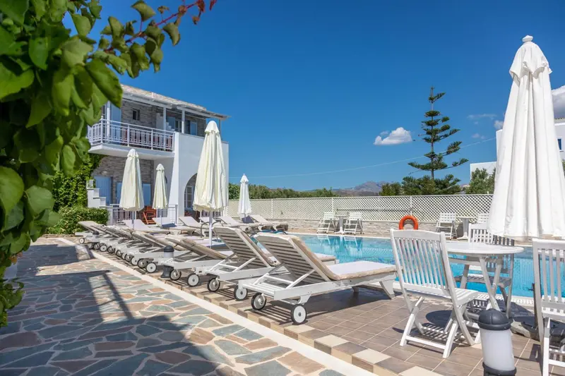 Transats blancs alignés au bord d'une piscine ensoleillée devant un bâtiment blanc.
