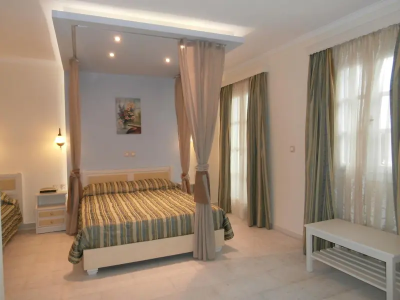 Une chambre lumineuse avec un grand lit à baldaquin et des rideaux décoratifs.