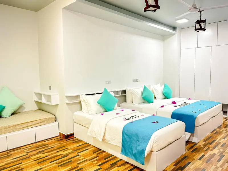 Une chambre lumineuse avec deux lits simples décorés de coussins turquoise.