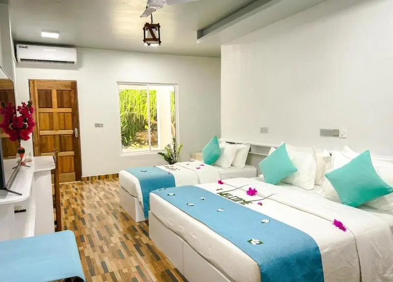 Chambre lumineuse avec deux lits simples décorés de coussins turquoise et de fleurs.