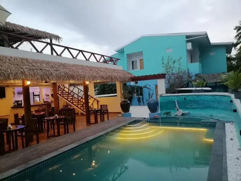 Une piscine turquoise bordée d'une terrasse en bois et d'un bar couvert.