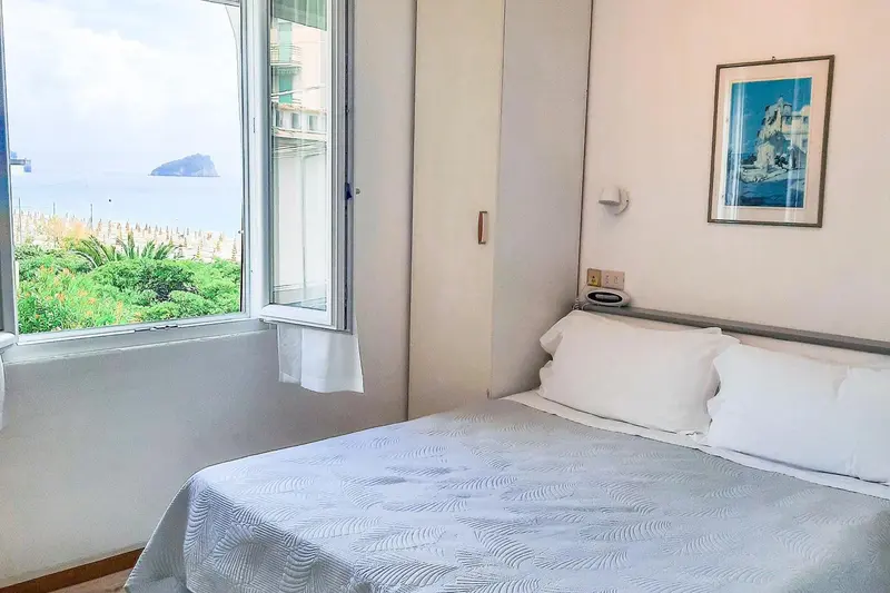 Une chambre lumineuse avec un lit fait et une vue sur la mer.