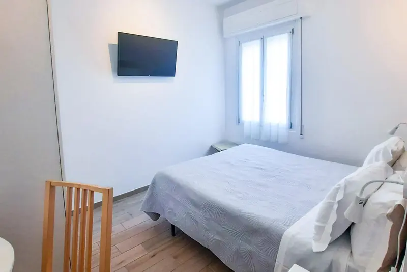 Une chambre lumineuse avec un lit et une télévision murale.