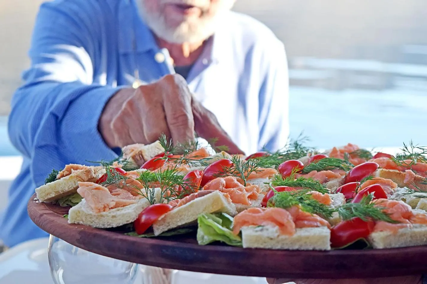 Une personne présente une assiette de sandwichs garnis de saumon et décorés de tomates cerises et d'aneth.