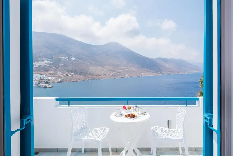 Vue sur la mer et les montagnes depuis une terrasse avec une table et des chaises.