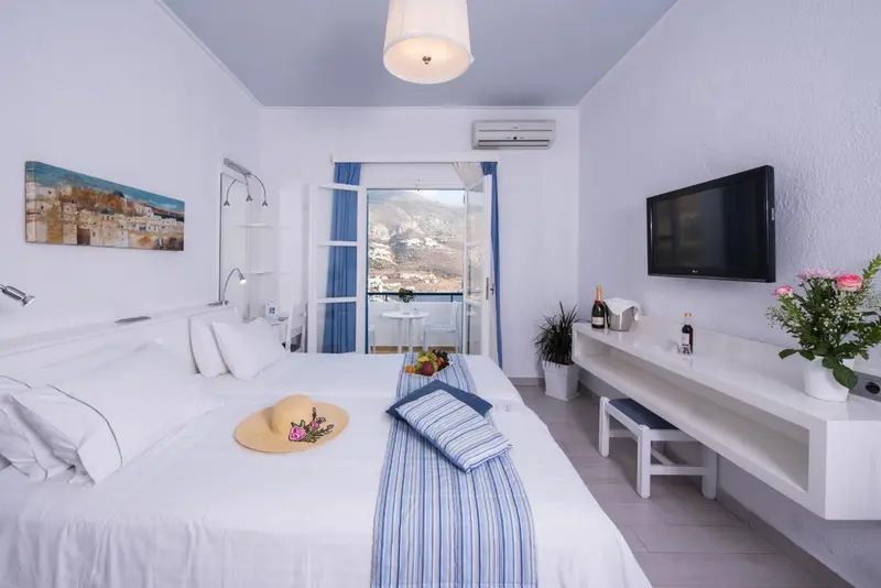 Chambre lumineuse avec un lit fait et une vue sur la mer par une baie vitrée.