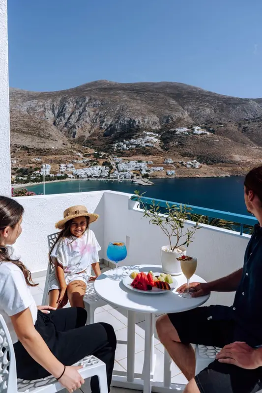 Une famille profite d'une collation sur une terrasse ensoleillée avec vue sur la mer et les montagnes.
