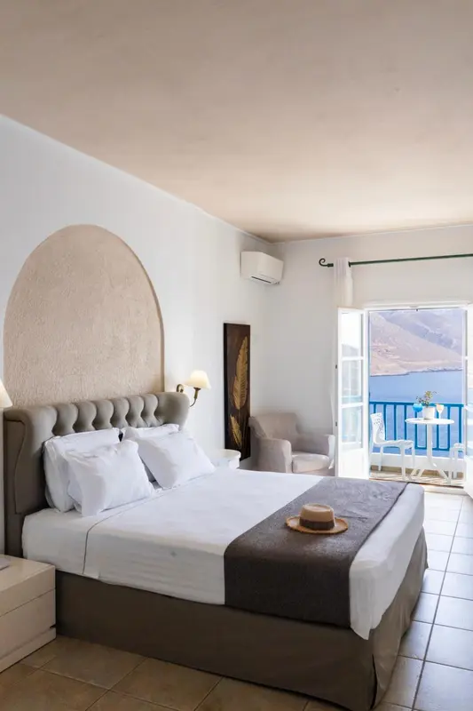 Une chambre lumineuse avec un grand lit et un balcon offrant une vue sur la mer.