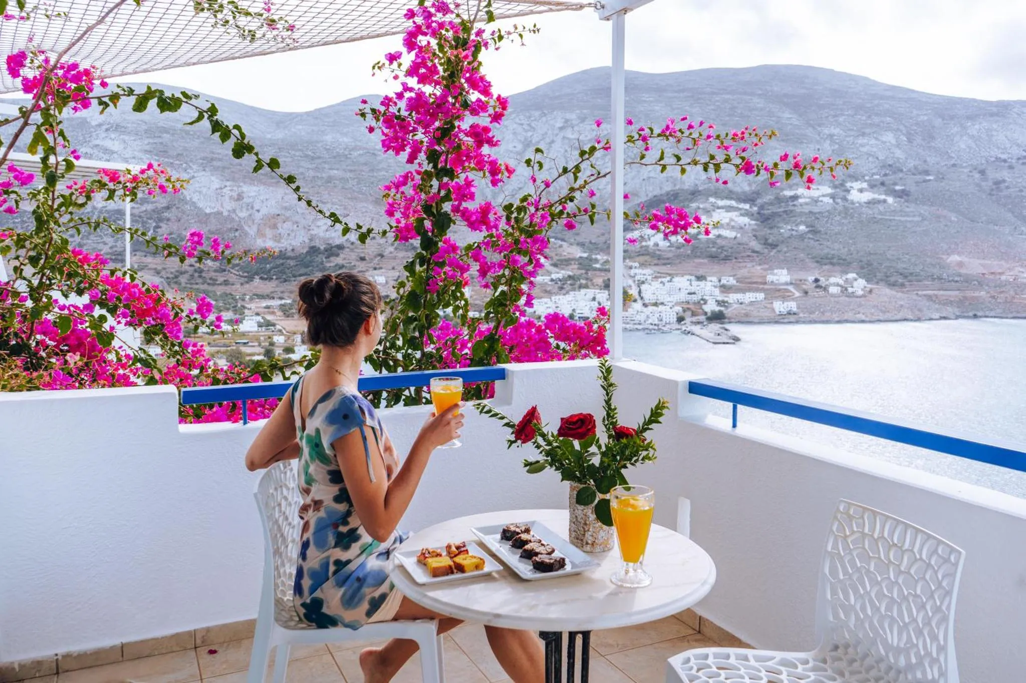 Une personne déguste une boisson et des pâtisseries sur une terrasse avec vue sur la mer et les montagnes.
