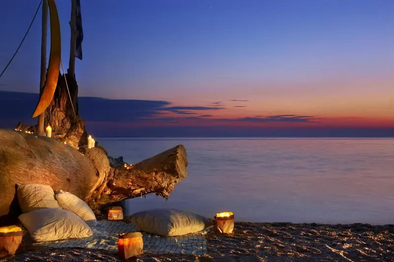 Coussins et lanternes disposés sur le sable au coucher du soleil.