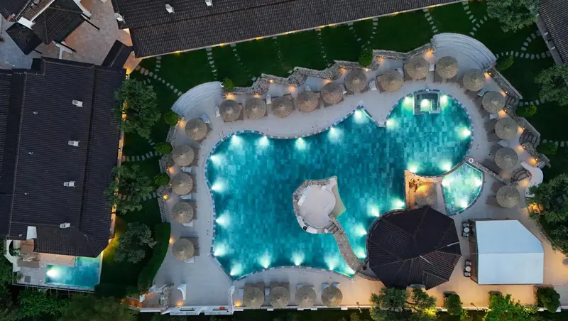 Vue aérienne d'une piscine sinueuse bordée de transats et de parasols.