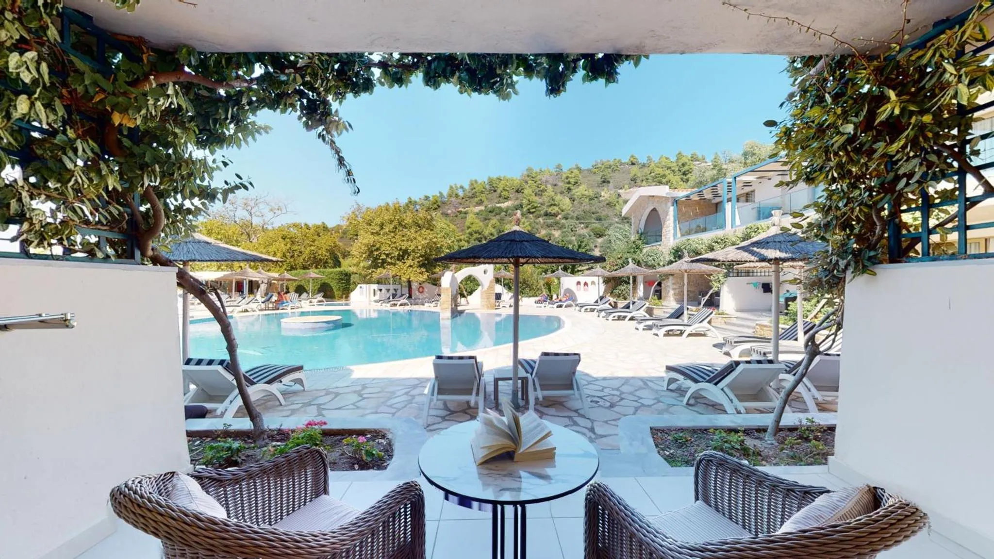 Terrasse ombragée avec mobilier de jardin donnant sur une piscine et des transats.