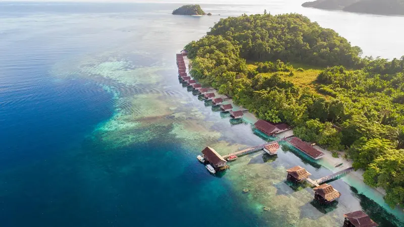 Vue aérienne d'une côte bordée de bungalows sur pilotis au-dessus d'eaux turquoise.