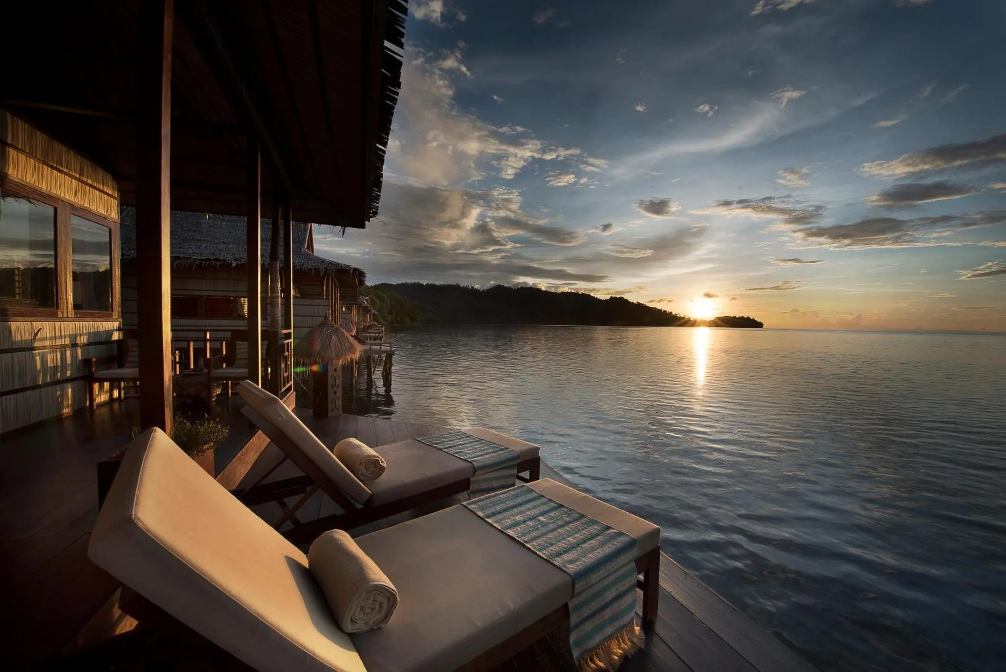 Terrasse avec transats donnant sur la mer au coucher du soleil.