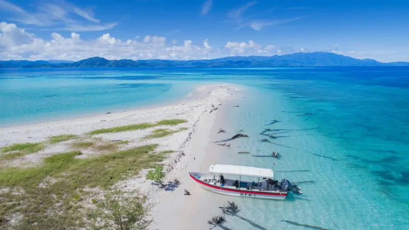 Vue aérienne d'une plage de sable blanc et d'une eau turquoise avec un bateau à moteur.