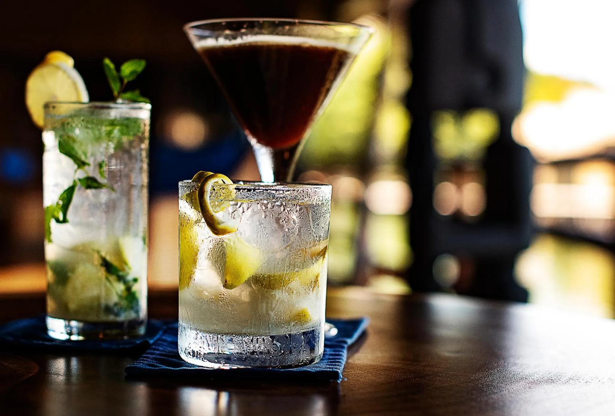 Trois verres de cocktails colorés sont présentés sur une table sombre.