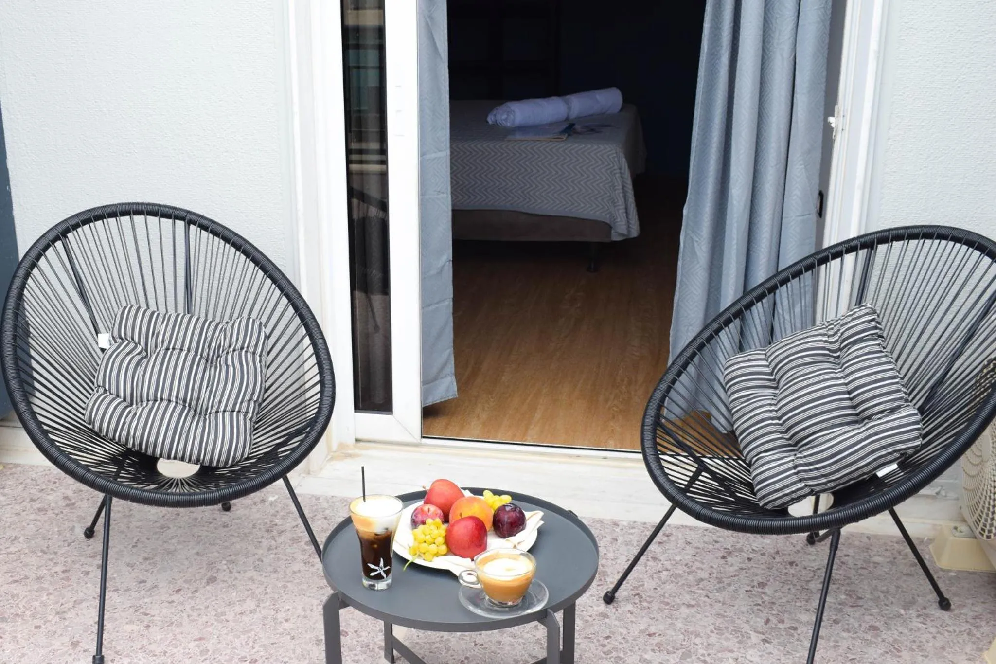 Deux fauteuils en osier et une table basse avec des fruits et des boissons sur une terrasse.