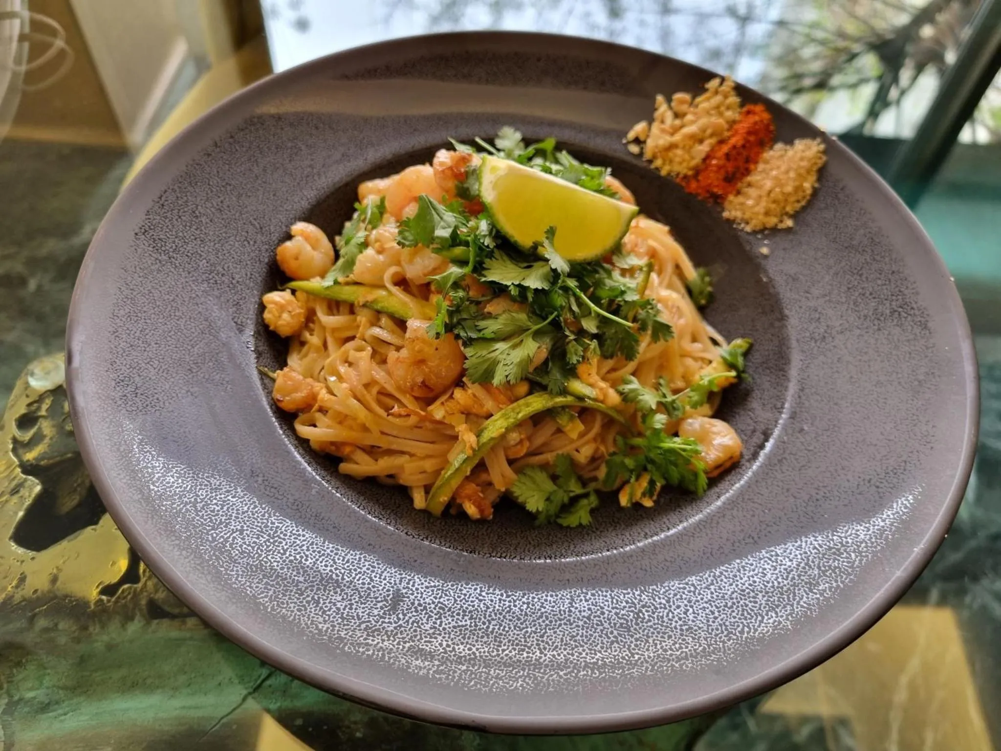 Assiette de nouilles aux crevettes garnie de coriandre et de citron vert.