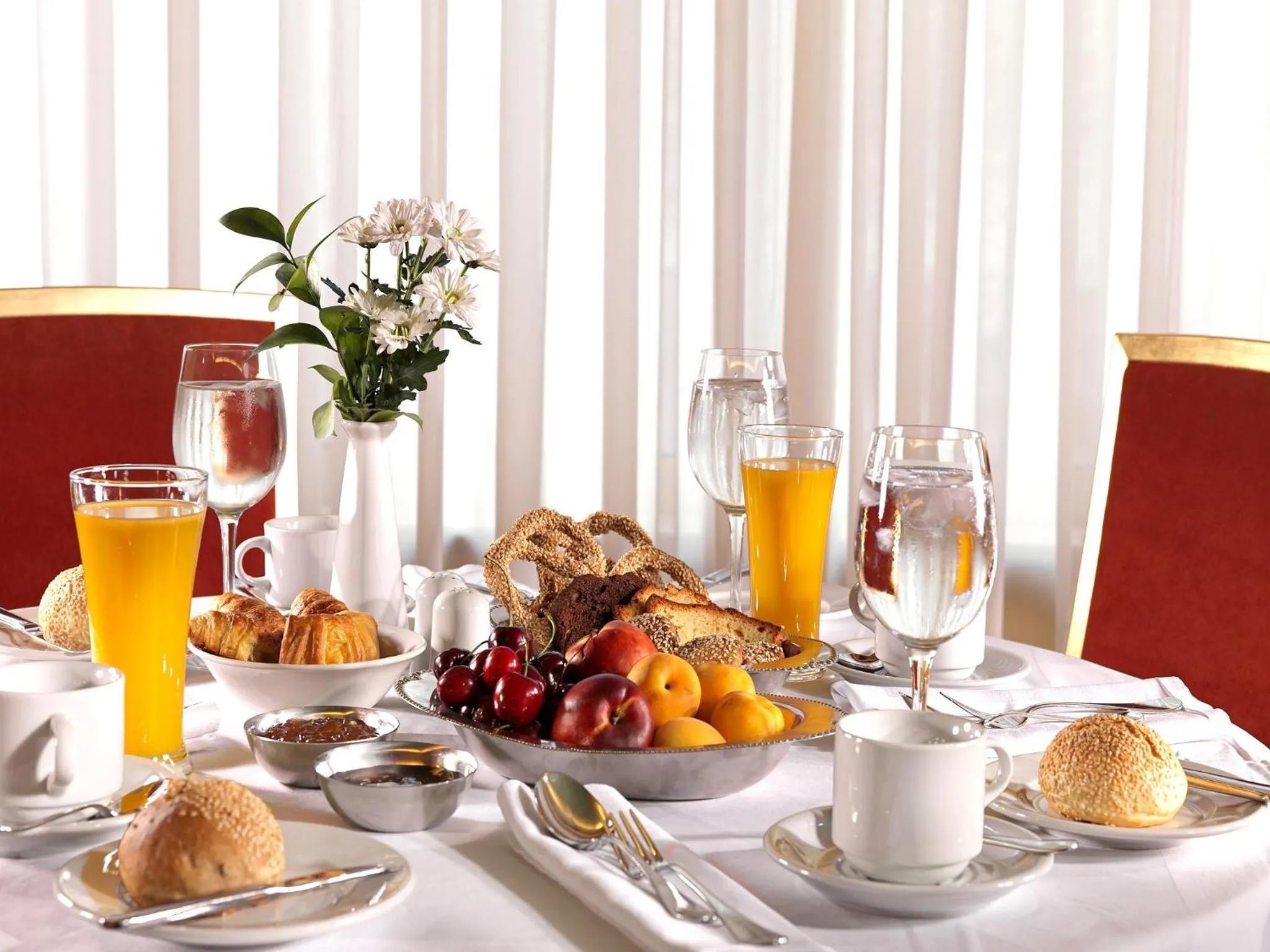 Une table est dressée pour le petit-déjeuner avec des viennoiseries, des fruits et des boissons.