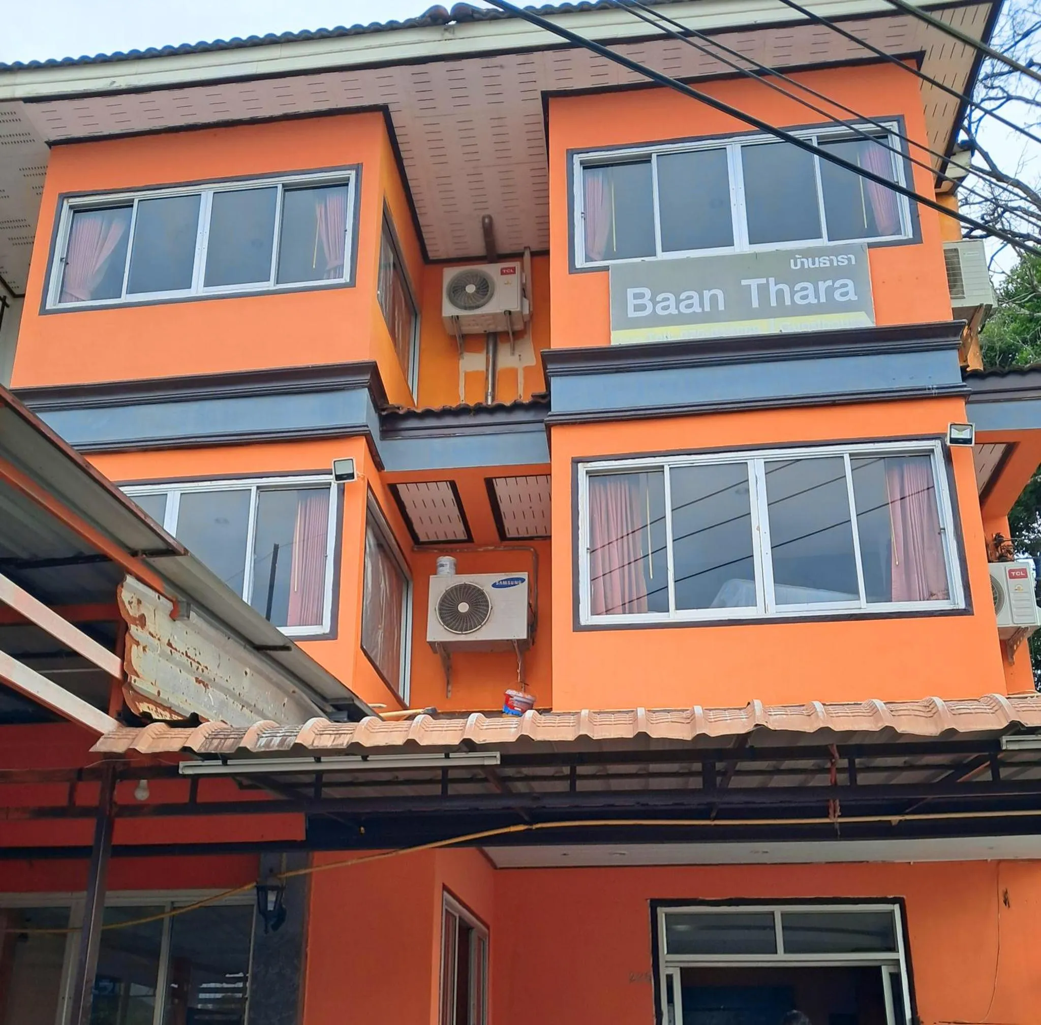 Facade d'un bâtiment orange à deux étages avec des fenêtres et des unités de climatisation.
