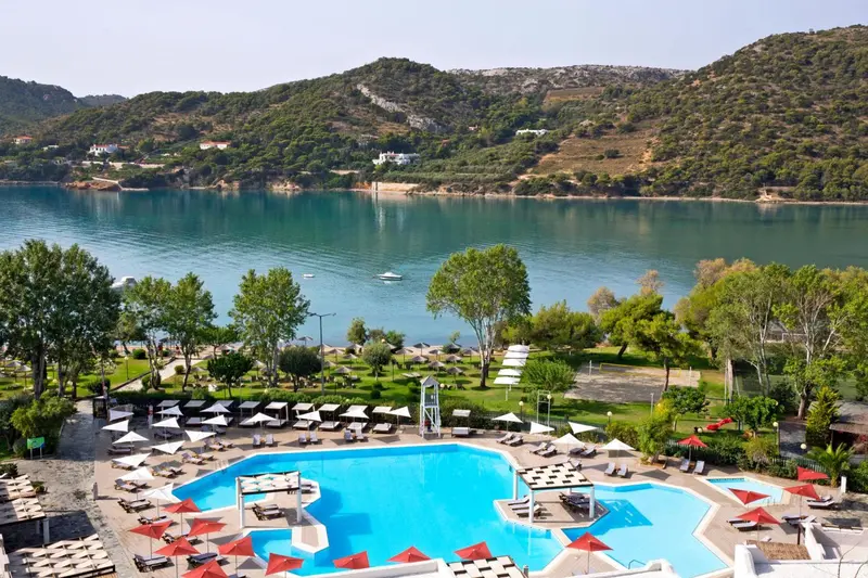 Vue aérienne sur une piscine d'hôtel bordée de transats, avec la mer en arrière-plan.