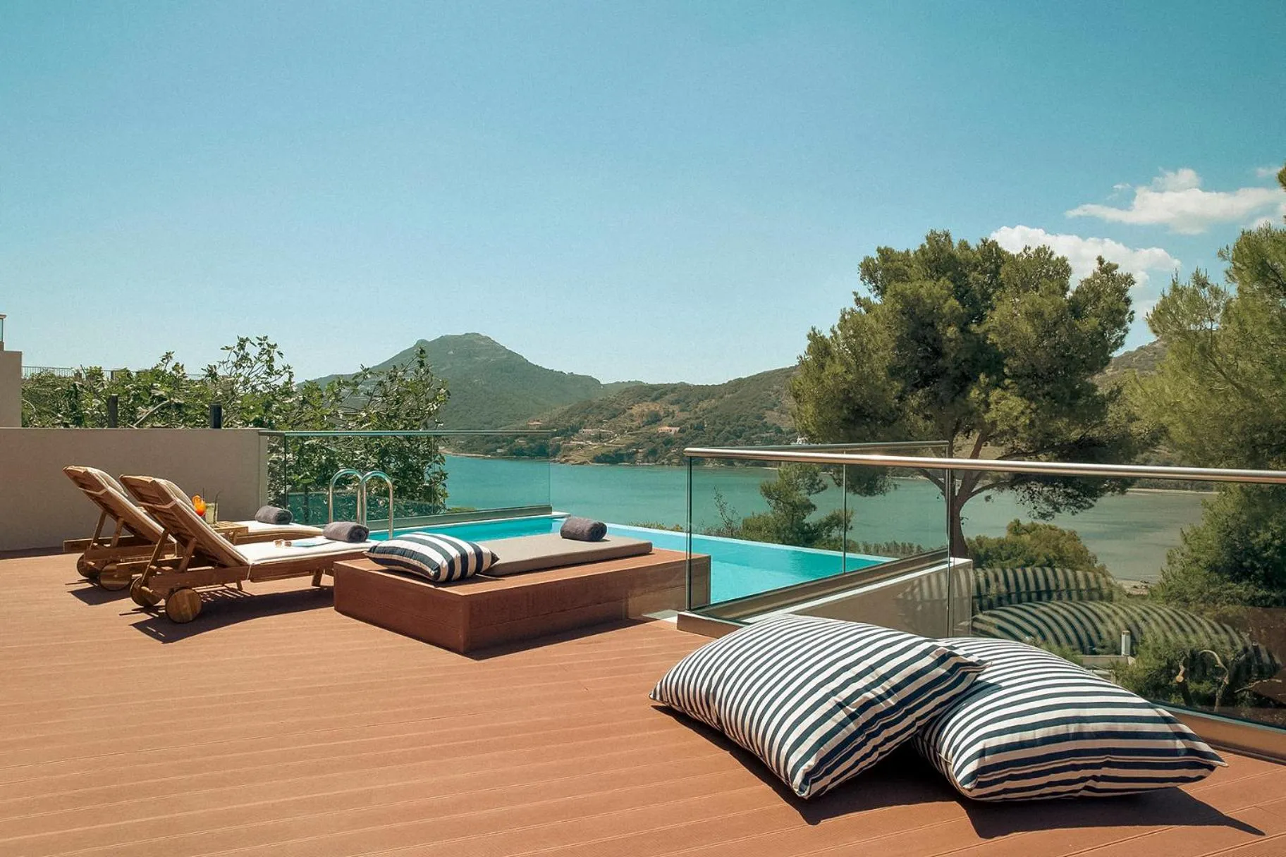 Terrasse avec chaises longues et piscine offrant une vue sur la mer et les collines.
