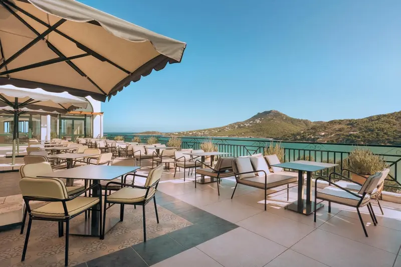 Terrasse ombragée avec tables et chaises donnant sur la mer et les collines.