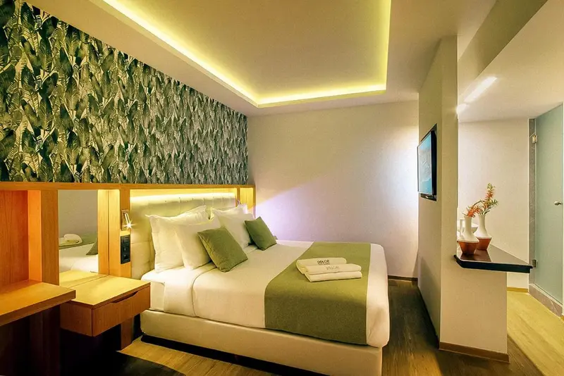 Une chambre lumineuse avec un grand lit et un mur décoré de motifs végétaux.