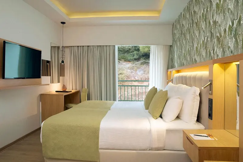 Chambre lumineuse avec un grand lit et une vue sur la végétation.