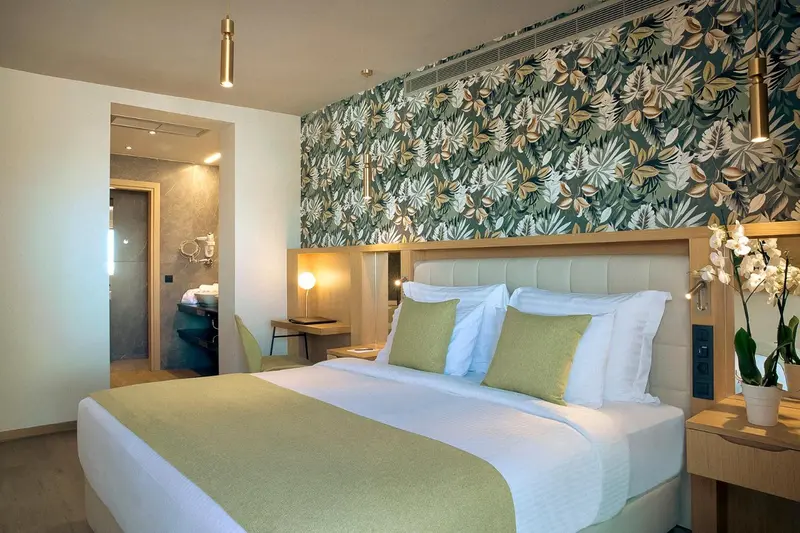 Une chambre lumineuse avec un grand lit et un mur décoré de motifs végétaux.