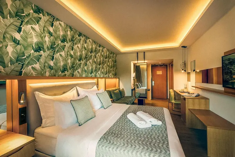 Une chambre lumineuse avec un grand lit et un mur décoré de motifs de feuilles.